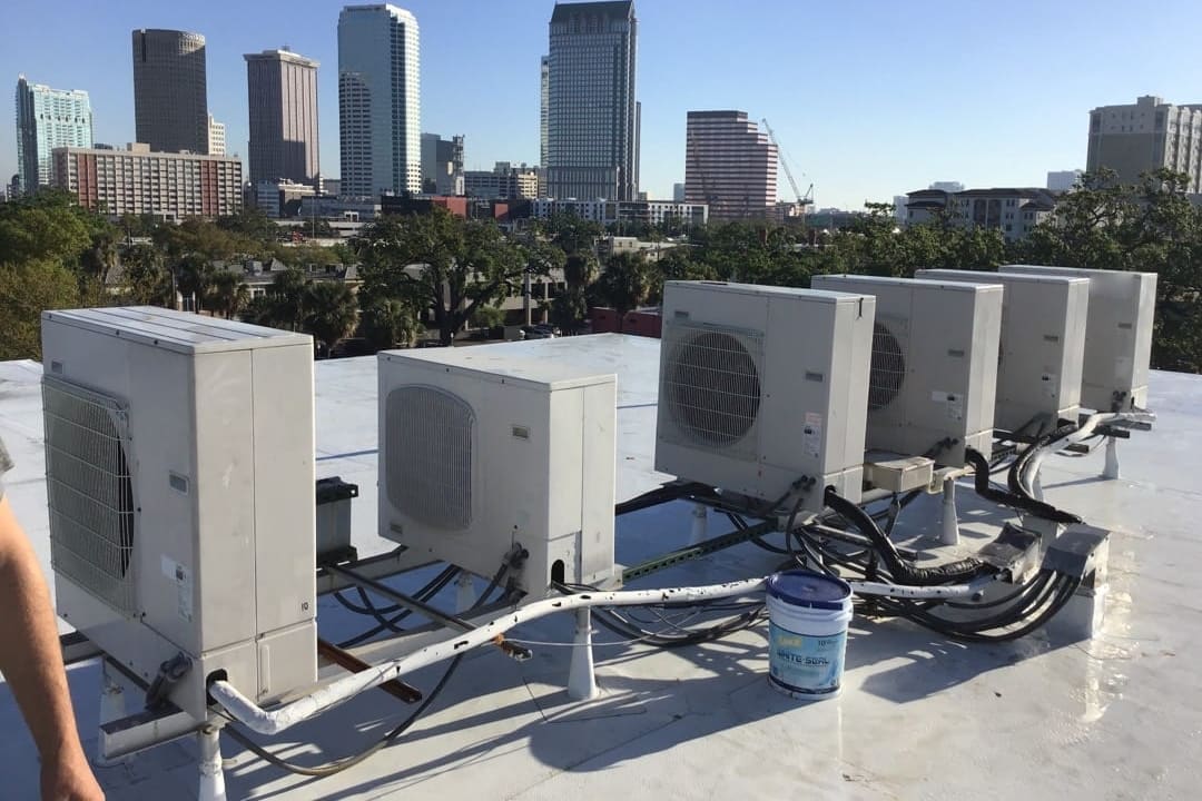A row of ductless outdoor units on a flat roof with the Tampa skyline behind them.