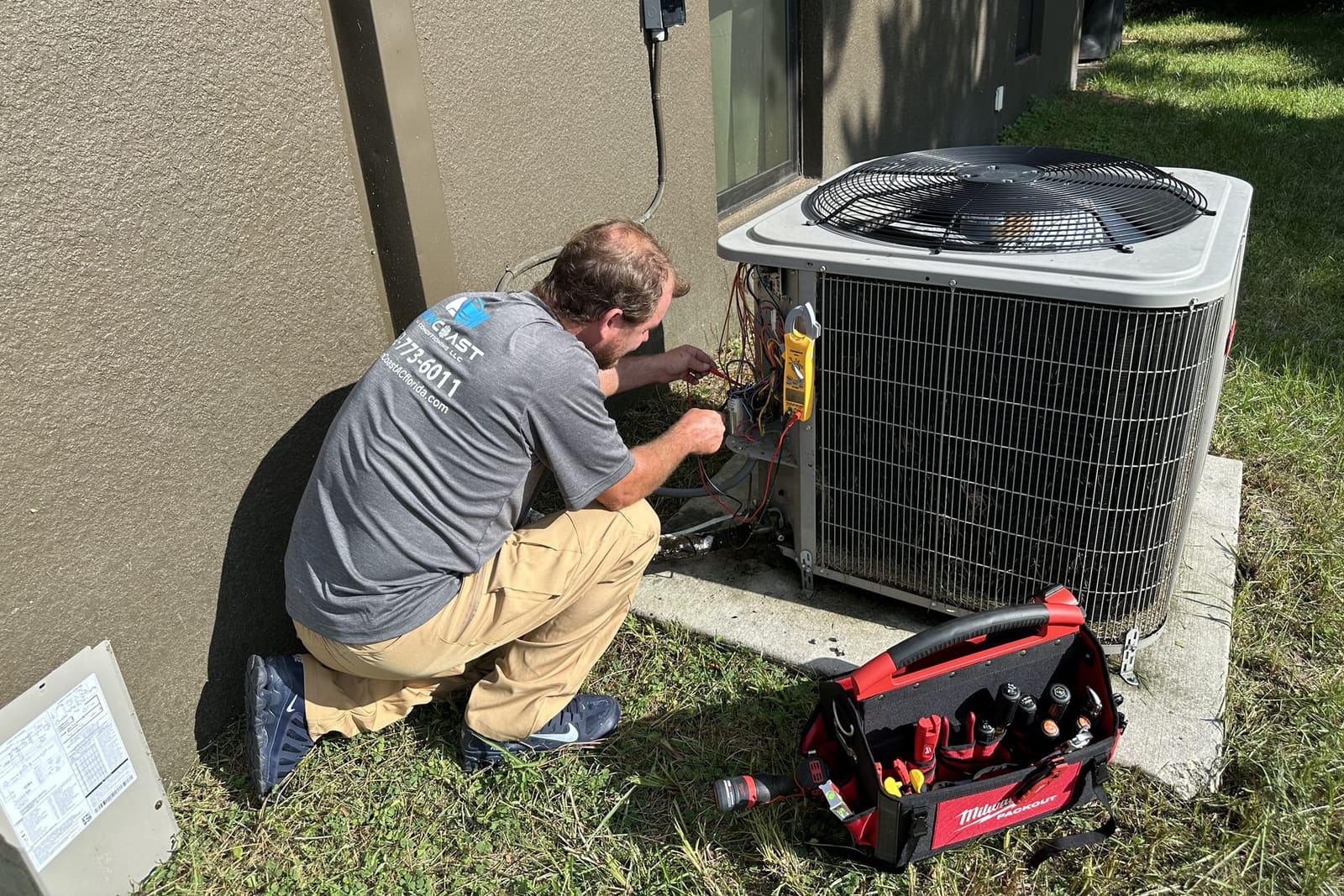 A SunCoast technician kneeling at an outdoor condenser beside a red tool bag in Spring Hill, FL.