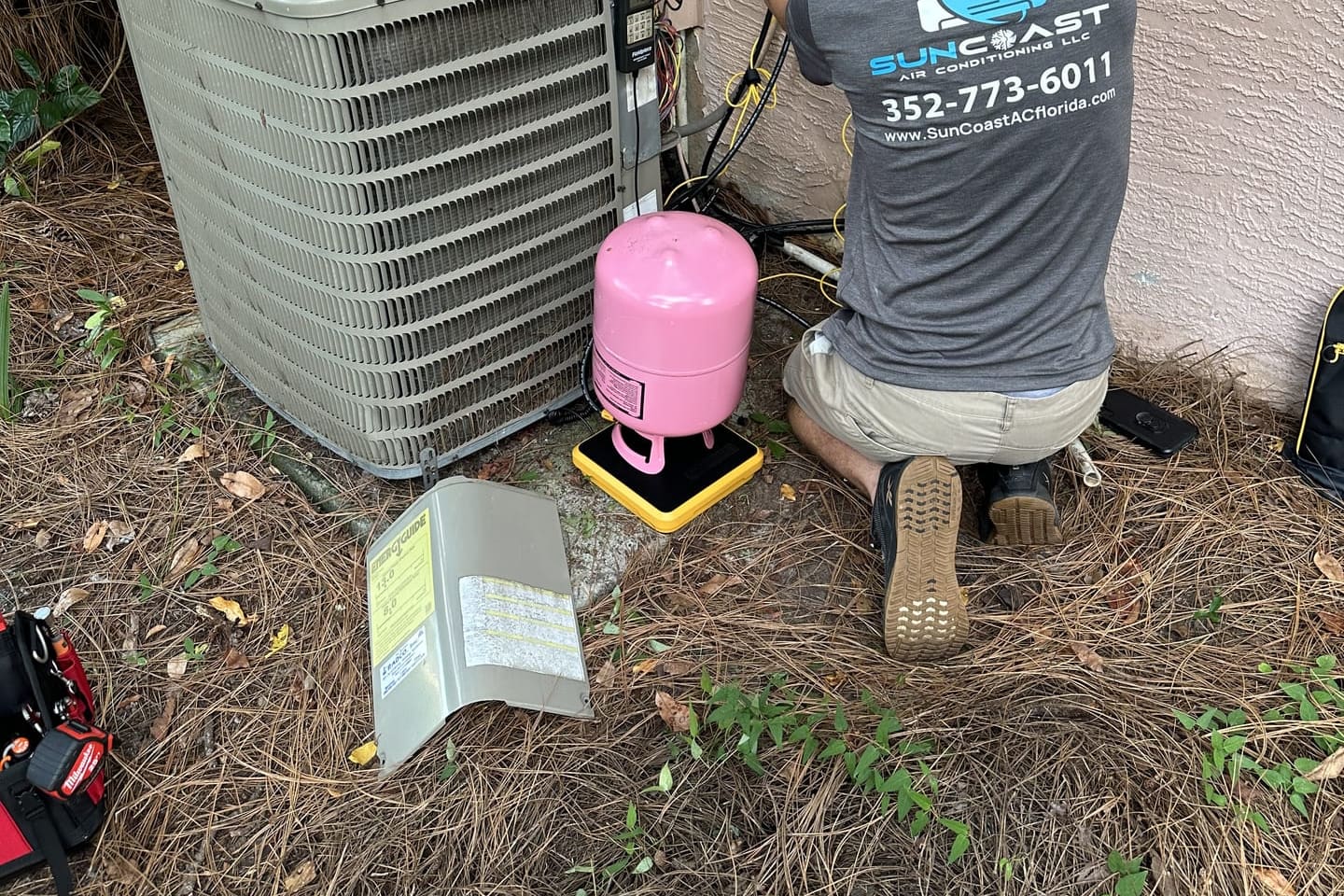 A SunCoast technician working at an outdoor condenser with a refrigerant cylinder beside him in Spring Hill, FL.
