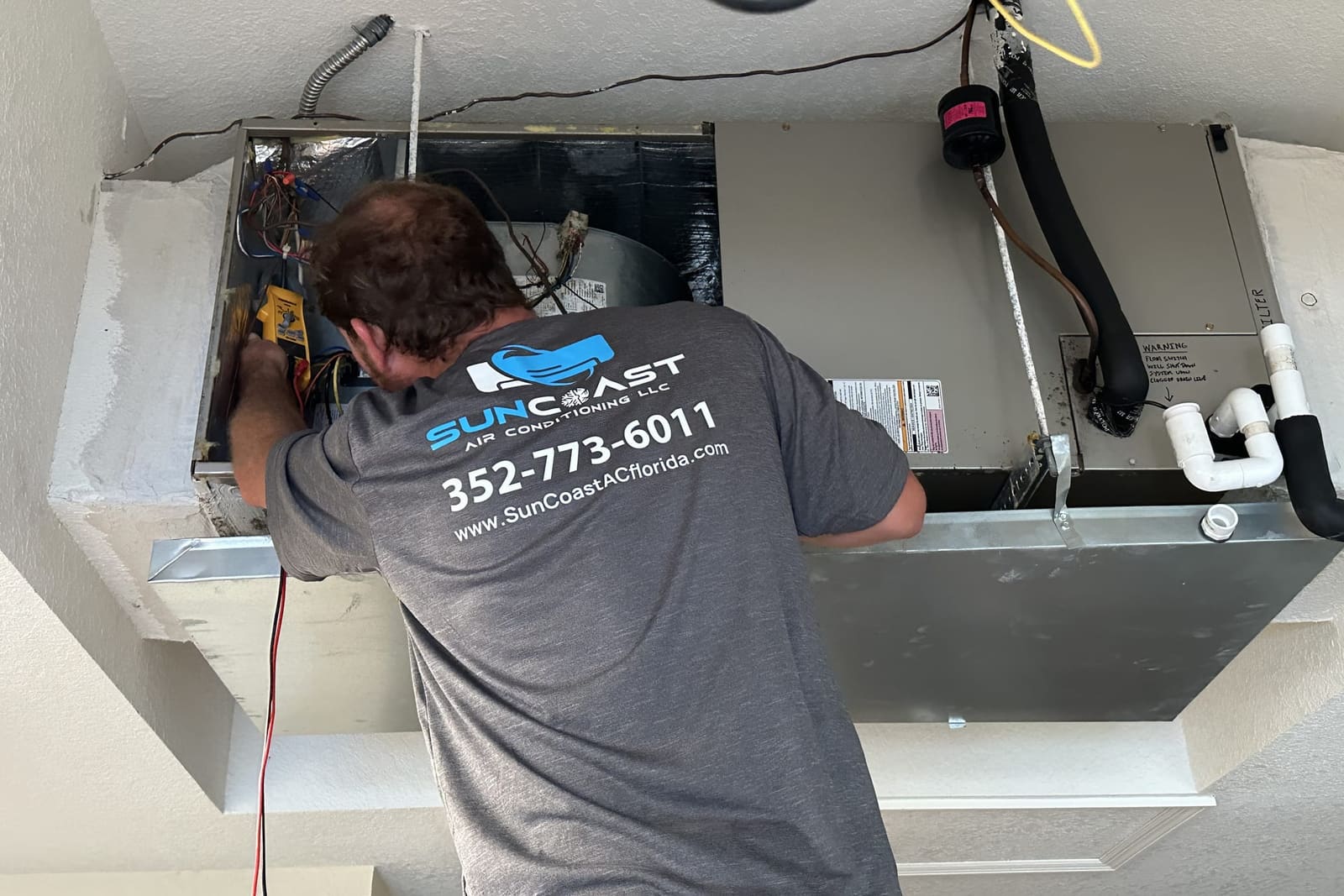 A SunCoast technician working over an air handler drain pan in Spring Hill, FL.