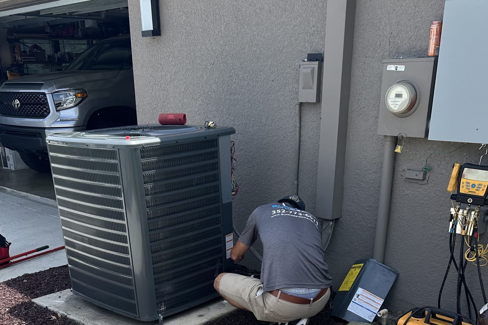 A technician kneeling at an outdoor condenser with test meters laid out on the ground in Pasco County, FL.